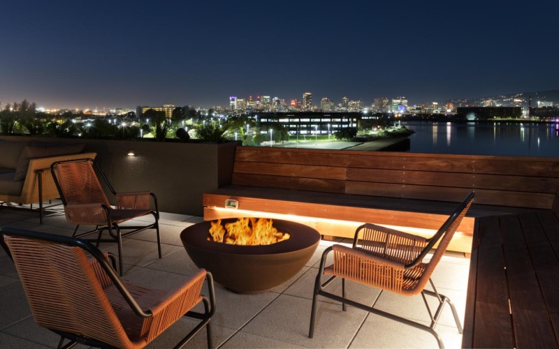 a table with chairs and a fire pit on a deck overlooking a city